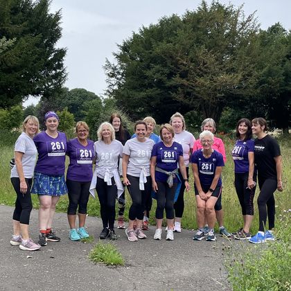 Group photo of women from the 261 Fearless running group on a country path, in a mixture of summer and sportswear, emphasised by a natural, green landscape in the background