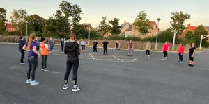 A group of women in sportswear doing a warm-up workout in a schoolyard at sunset, showing commitment and team spirit