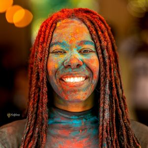 Eine Frau mit einem strahlenden Lächeln und buntem Farbpulver im Gesicht, ein lebendiges Bild, das Freude und Feierlichkeit bei einem 261 Fearless Event vermittelt