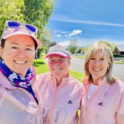 Three beaming 261 Fearless women in matching pink Adidas running jackets take a selfie, with a sunny, green landscape background