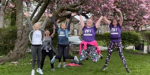 Women of the 261 Fearless running group jumping joyfully under a flowering tree, in a line, in casual wear, symbolising joy and energy