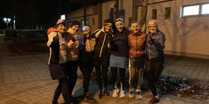Frauenlaufgruppe bei 261 Fearless in Winterlaufkleidung, die nachts auf einer beleuchteten Straße für ein Foto posieren, strahlend vor Freude nach einem gemeinsamen Lauf