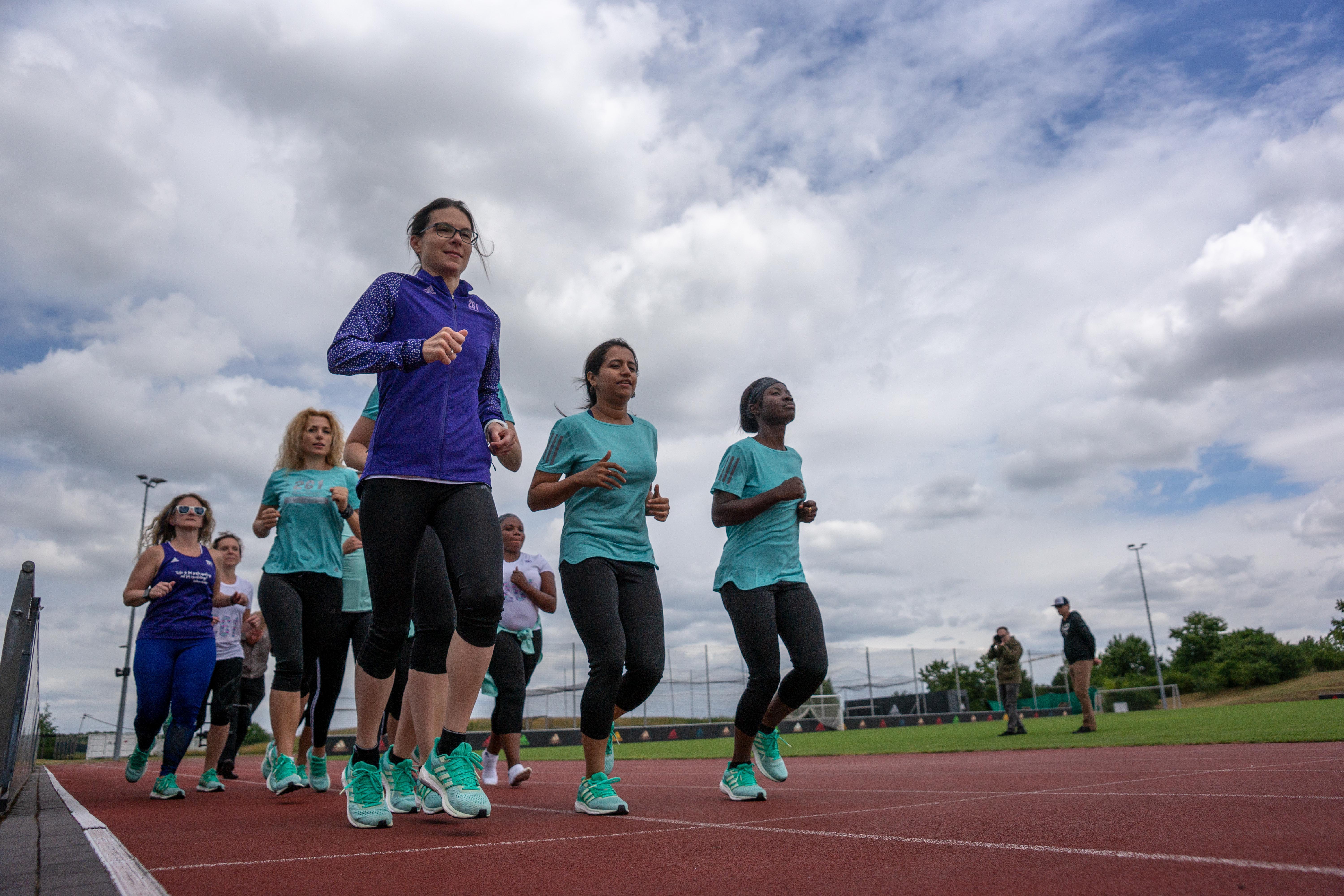 Women of the 261 Fearless running group in action on a running track, photographed under a cloudy sky during a training run