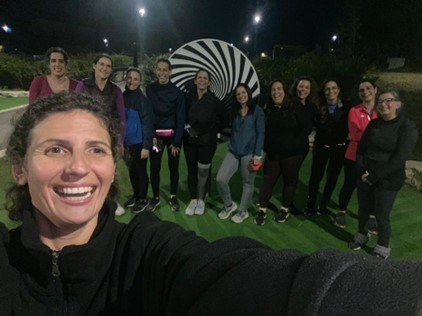 Group picture of women from the 261 Fearless running group posing on an illuminated mini golf course