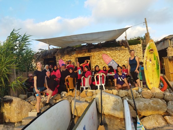Members of the 261 Fearless women's running group stand next to surfboards on a rocky beach and smile for the camera