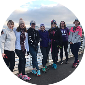 Group photo of six women from the 261 Fearless women's running group on a bridge, standing in a row, overlooking a waterfront